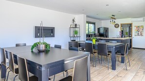 Una cocina moderna con una isla central, un comedor con una mesa grande y sillas, y una sala de estar con televisor y obras de arte en la pared.
