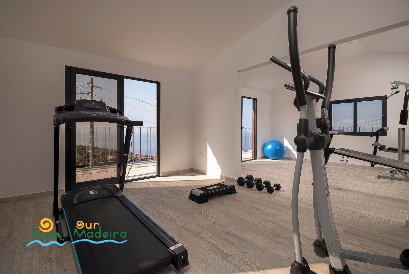 A spacious home gym with a treadmill, dumbbells, a bench press, and a rowing machine.