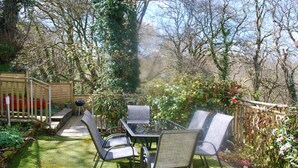Un patio con tavolo e sedie in vetro, circondato da un giardino con diverse piante e una recinzione in legno.