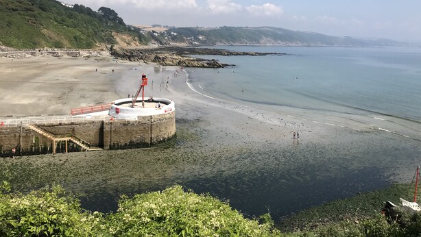 Una spiaggia costiera con un faro, scogliere rocciose e cielo sereno.