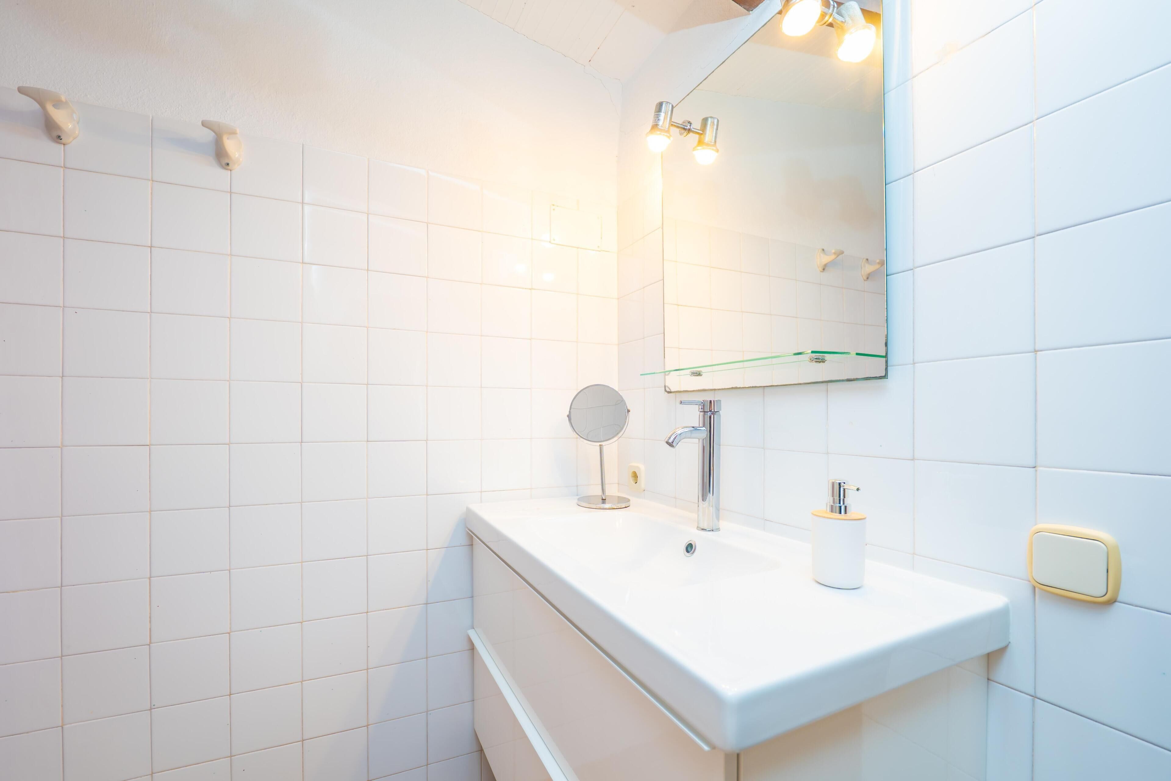 Une salle de bain avec des carreaux blancs, un lavabo, un miroir et un porte-serviettes.