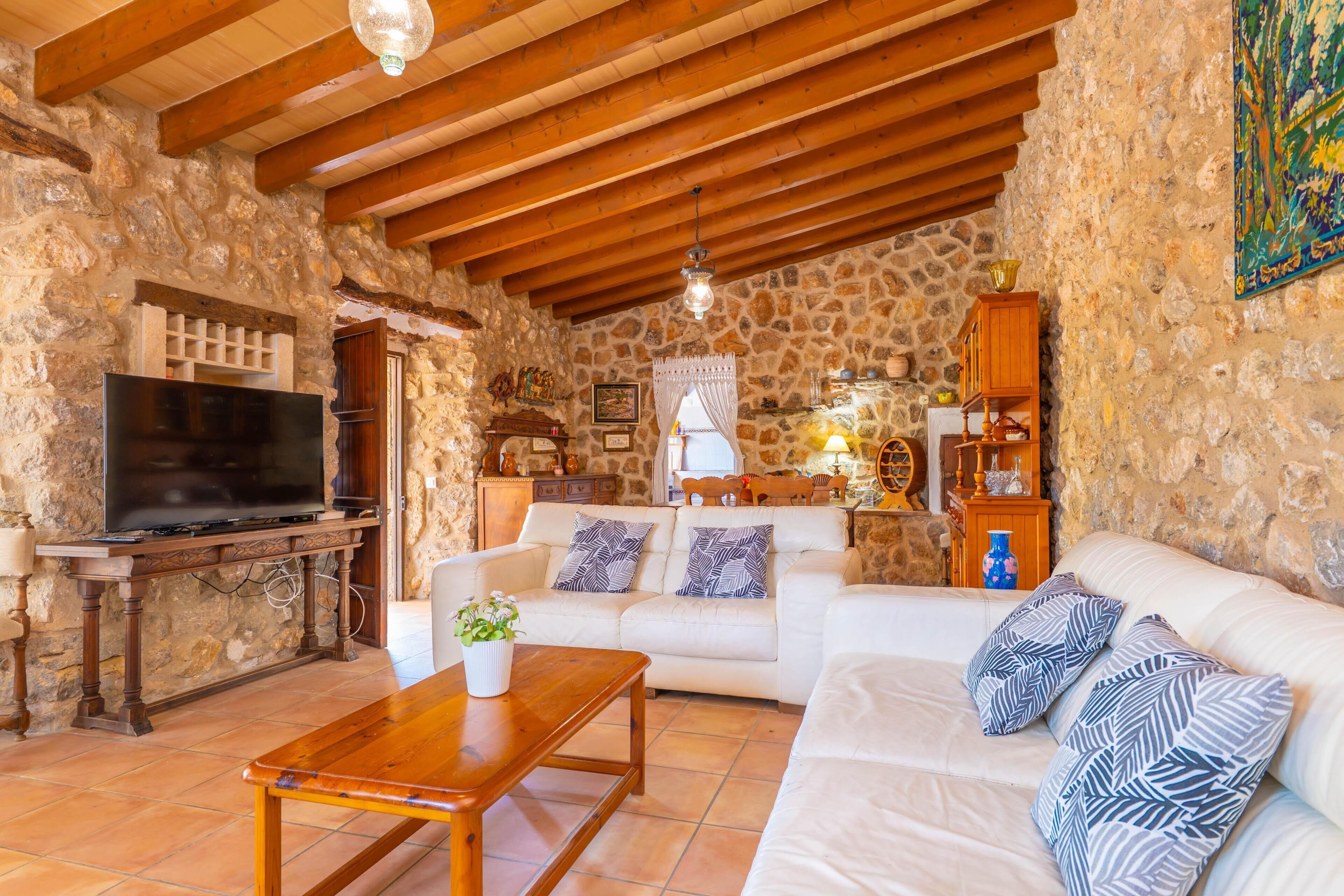 Una habitación con paredes de piedra y techo de madera, un televisor, un sofá, una mesa de centro y un jarrón decorativo.