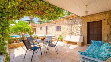 Un patio con mesa y sillas, un sofá y un muro de piedra.