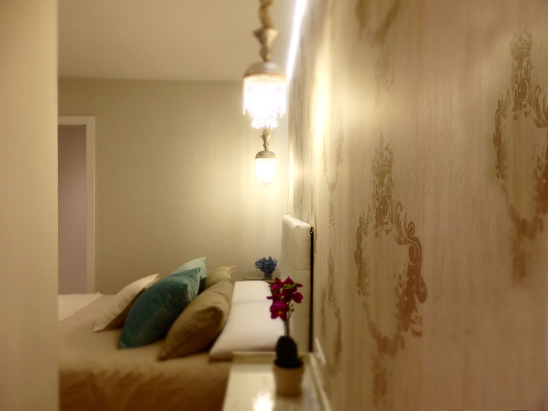 A bedroom with a bed, pillows, a nightstand, a lamp, and a wall with a floral pattern.