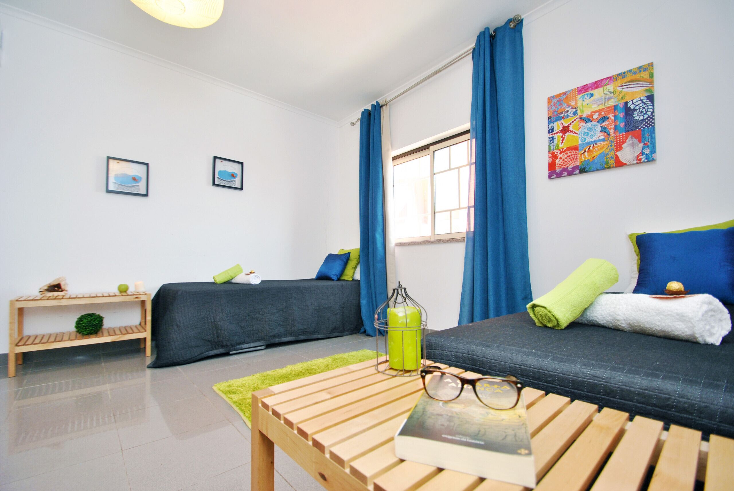 A modern, well-lit room with two beds, a wooden table, and a colorful artwork on the wall.