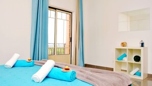 A hotel room with a bed, blue and white towels, a white shelf with decorative items, and a window with curtains. - Cozy Apartment w/ Pool in Albufeira (Albufeira)