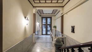 A marble-floored hallway with a wooden staircase, a double door with a metal gate, and wall-mounted sconces. - Luxurious Oasis Paseo de Gracia (Barcelona)