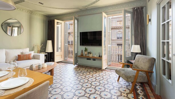 A hotel room with a sofa, a dining table set, a TV, and a patterned floor. - Luxurious Oasis Paseo de Gracia (Barcelona)