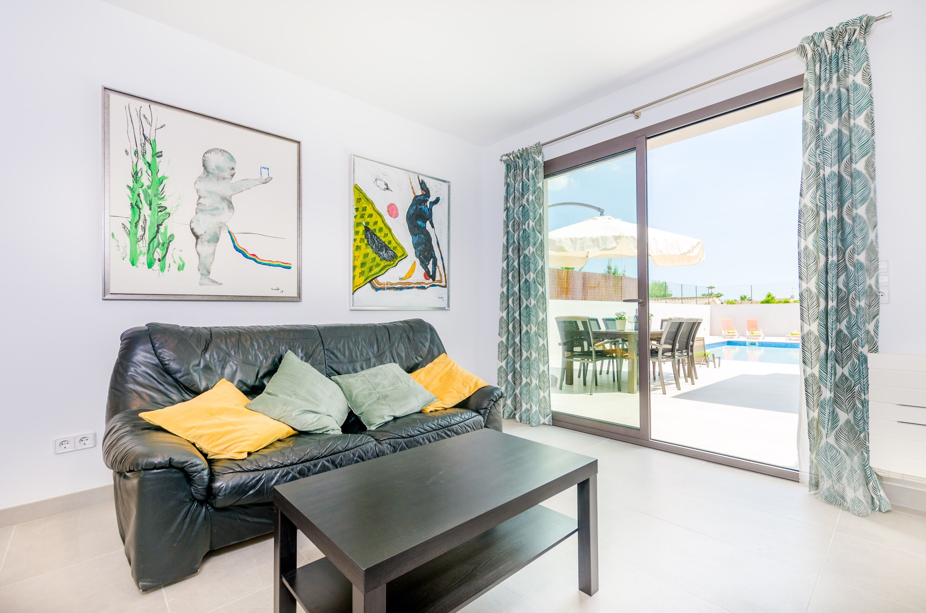 A modern living room with a black leather sofa, a coffee table, and two artworks on the wall.