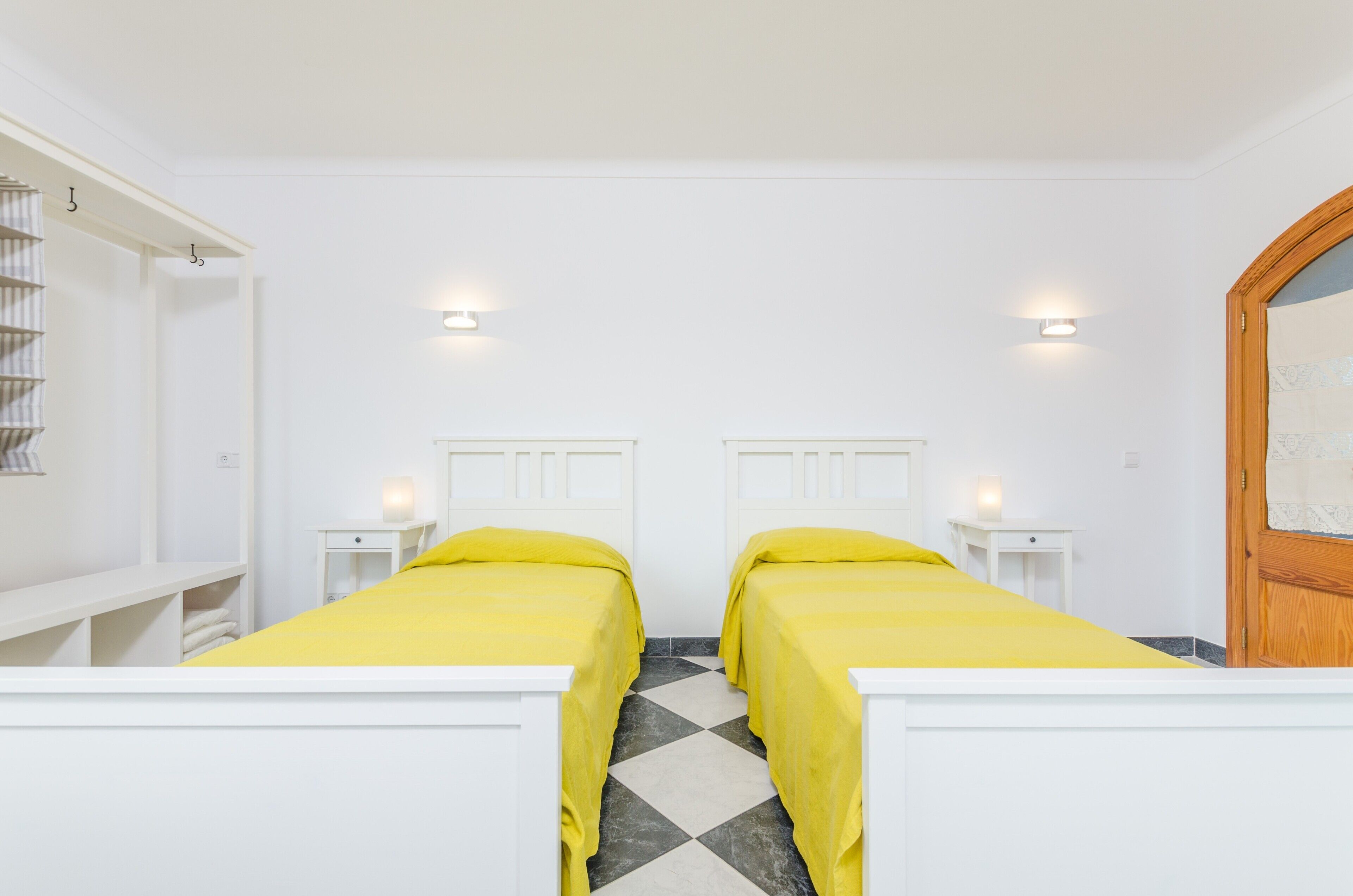 Habitación doble con dos camas, paredes blancas y suelo a cuadros.