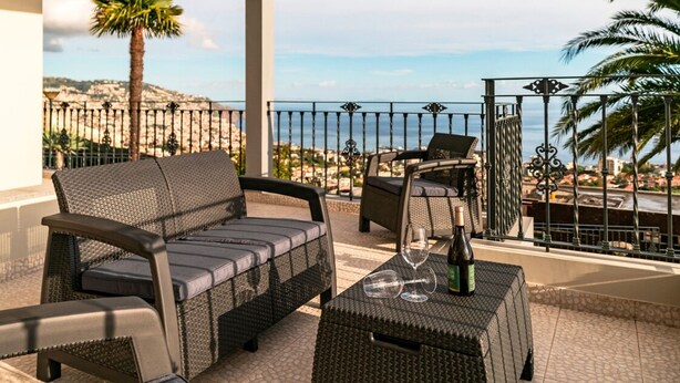 A balcony with wicker furniture, a glass table, and a view of the sea.