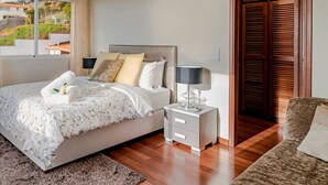 A neatly arranged bedroom with a bed, bedside table, and a view of the outside.