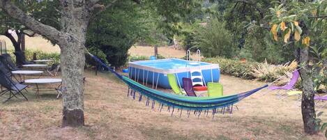Un hamac avec des fauteuils, une piscine et une table, le tout installé dans un jardin.