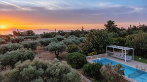 Area piscina con pergola e poltrone relax, circondata da ulivi e vista sul tramonto.