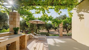 Un patio con un lavello in pietra, un tavolo di legno, una poltrona da relax e un ombrellone.