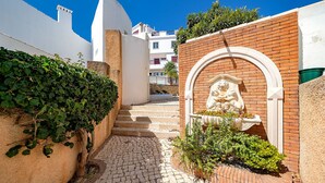 A narrow cobblestone pathway leading to a building with a white facade and a brick wall. A statue of a lion is visible in an arched niche. - Modern downtown apartment [28] (Lagos)