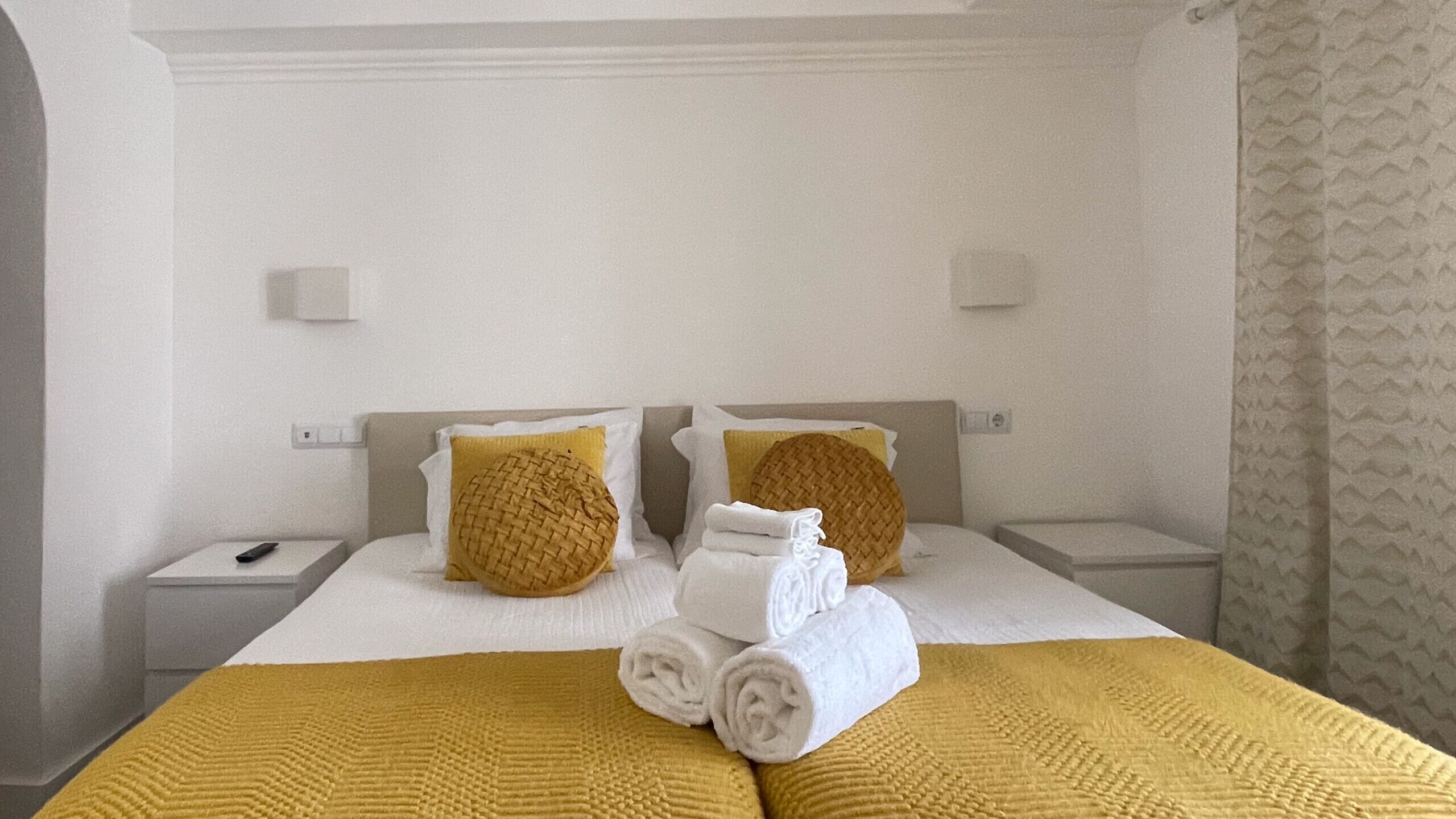 Een hotelkamer met een bed, twee nachtkastjes en een geel gebreid plaid.