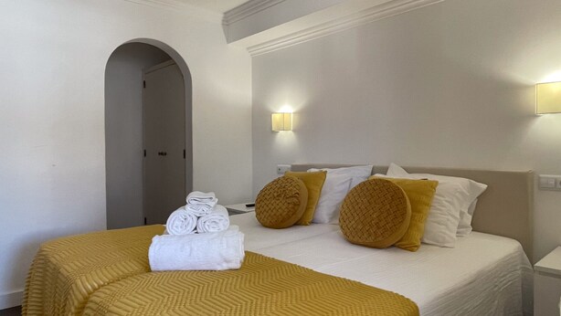 A hotel room with a bed, a rolled towel on the bed, a wall-mounted light, and a door. - Sofeelings Estudio Sol, Baixa de Albufeira (Albufeira)
