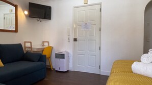 A room with a sofa, a chair, a bed, a TV, and a door with a notice. - Sofeelings Estudio Sol, Baixa de Albufeira (Albufeira)