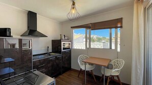 A compact kitchen with modern appliances, a dining area with two chairs, and a view of the city through large windows. - Sofeelings Estudio Sol, Baixa de Albufeira (Albufeira)