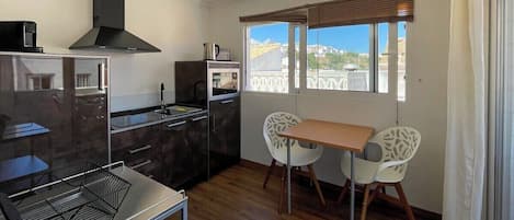 Een compacte keuken met moderne apparatuur, een eethoek met twee stoelen, en een stadszicht door grote ramen.