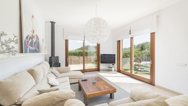 Una sala de estar moderna con un sofá modular, una mesa de centro de madera y una lámpara de araña grande. Se observa un televisor y una chimenea al fondo.