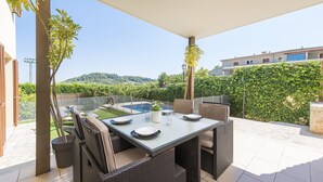 Un patio al aire libre con una mesa preparada para comer, rodeado de muebles de mimbre y vistas a una piscina y exuberante vegetación.
