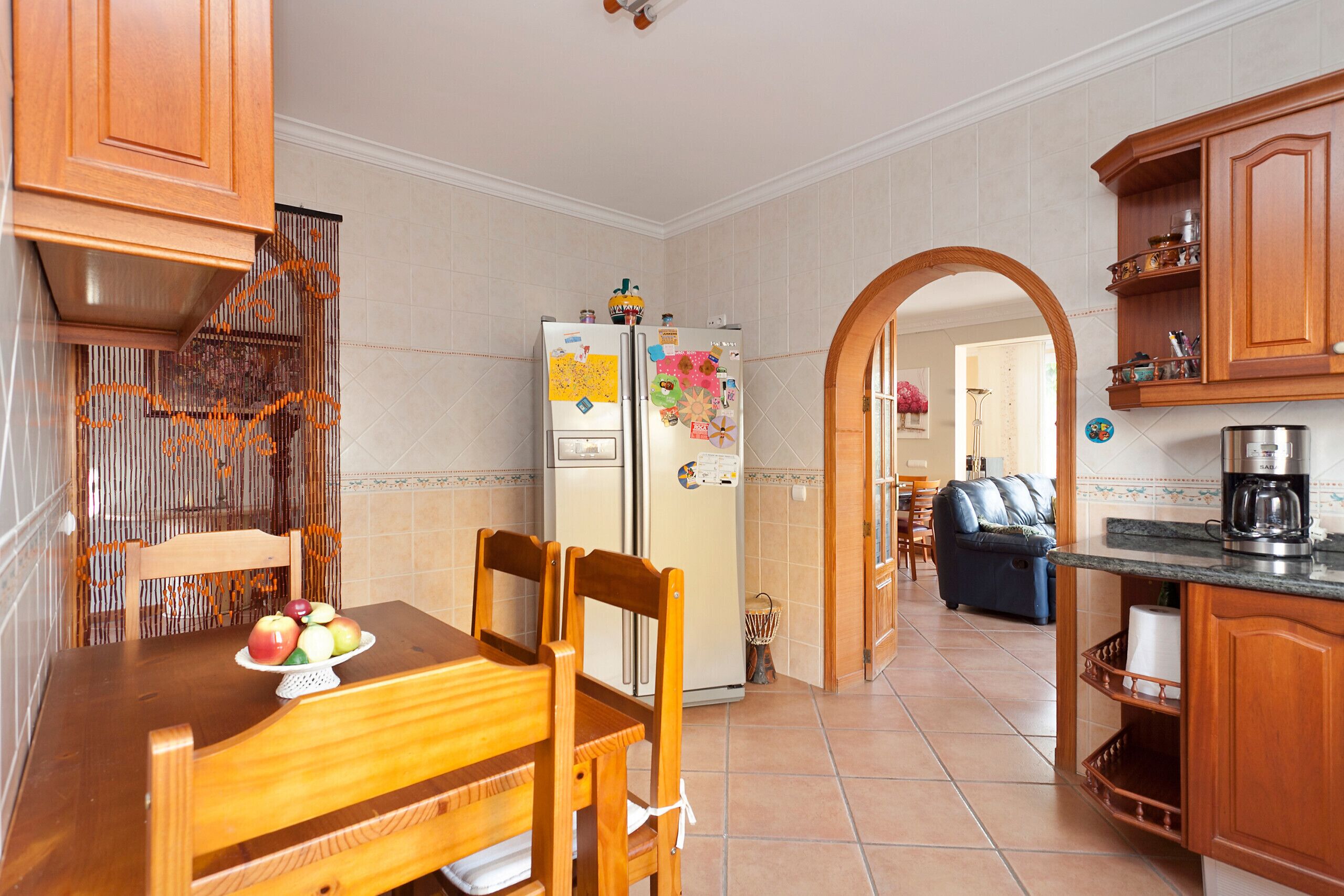 A kitchen with wooden cabinets, a refrigerator, a dining table with chairs, and a coffee maker.