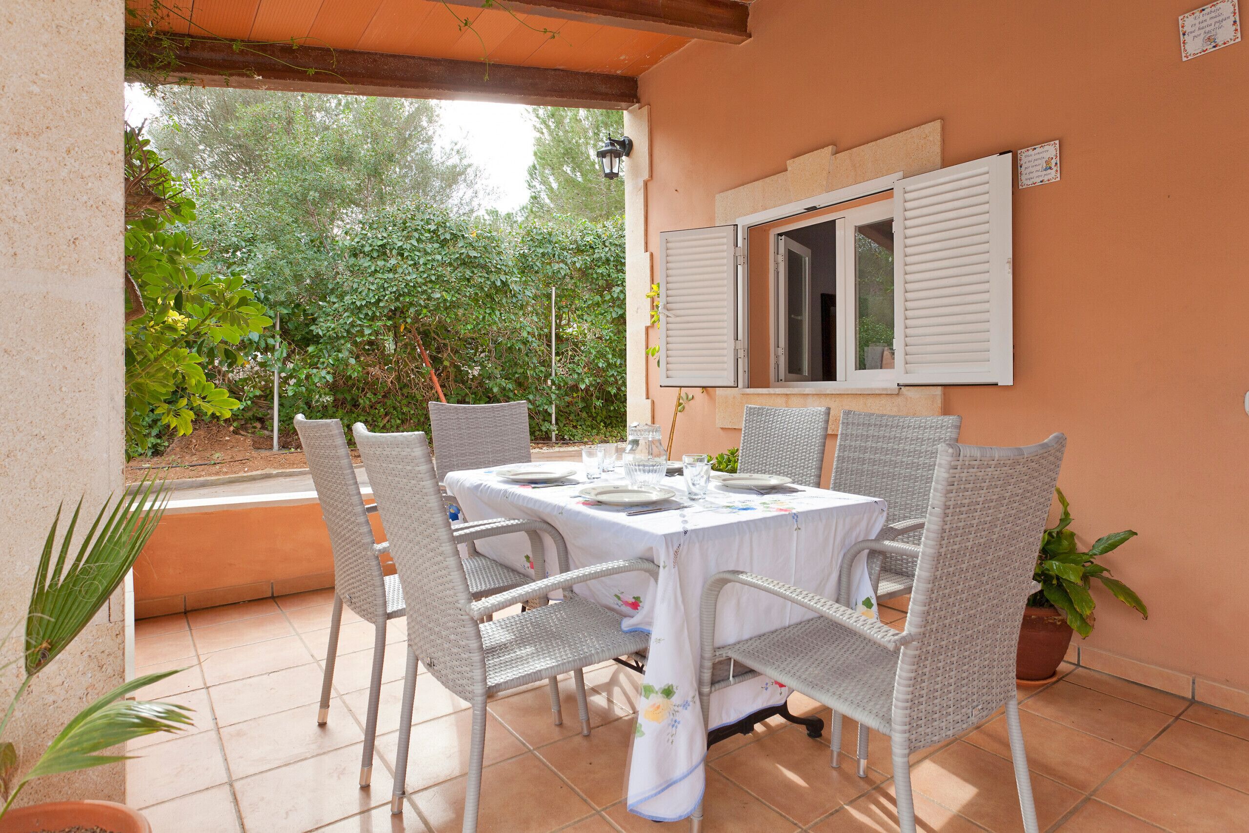 Un espace extérieur abrité, aménagé pour les repas, avec une table dressée pour quatre personnes, entourée de chaises en osier.