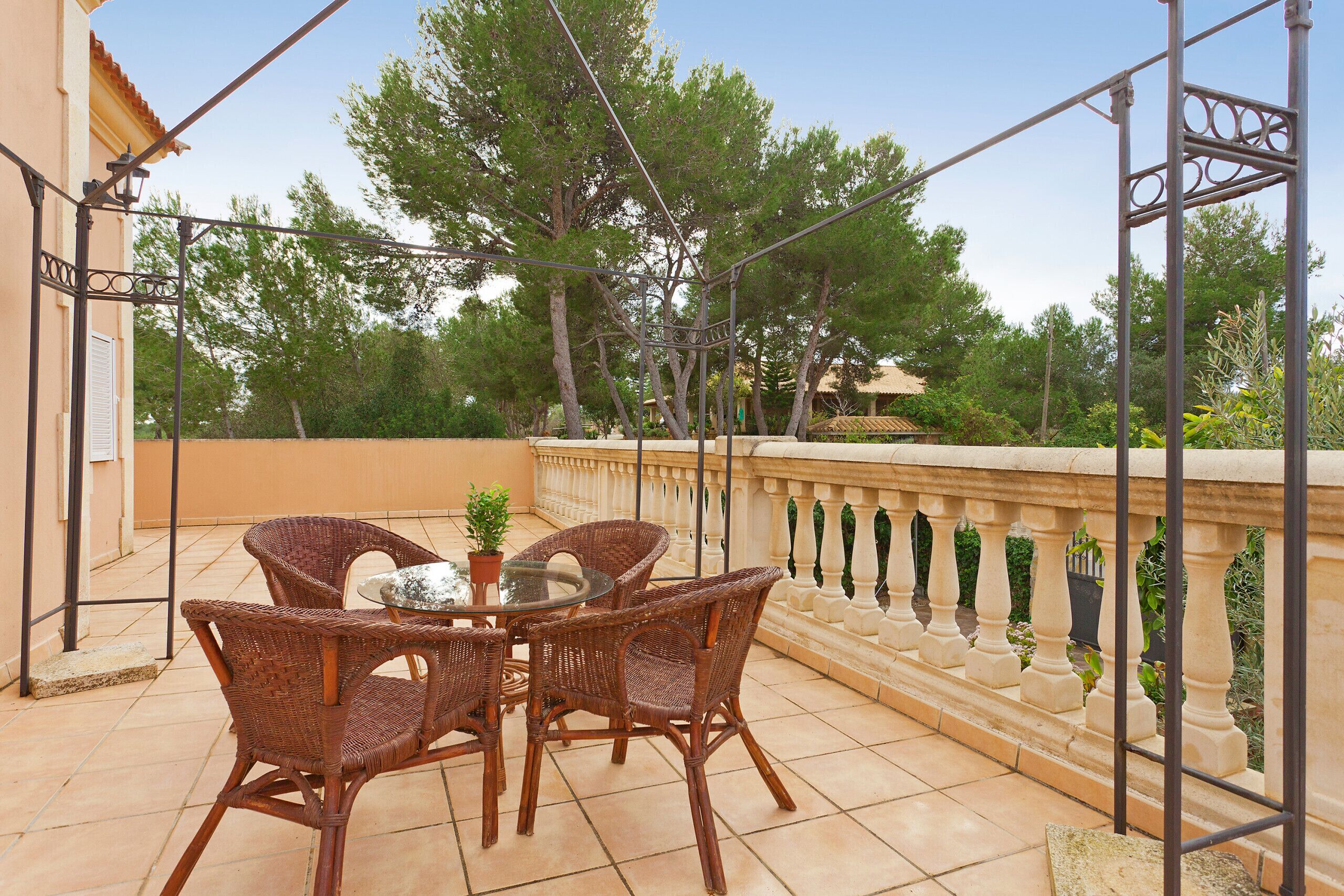A terrace with wicker chairs and a glass table, surrounded by a balustrade and trees.