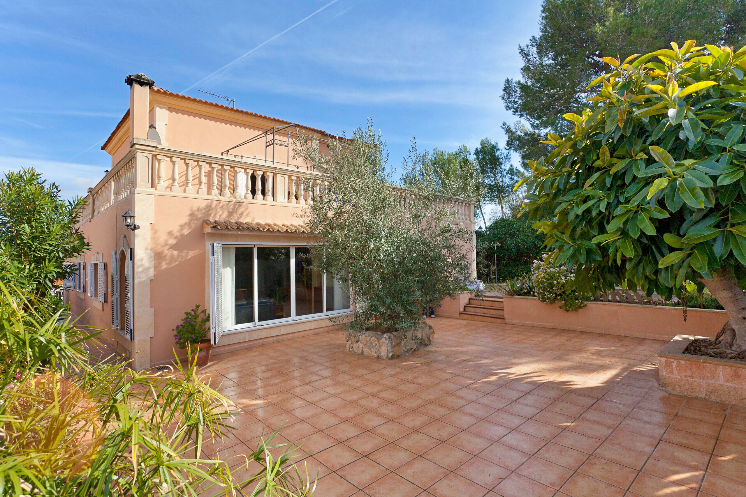 A house with a tiled patio, a balcony, and surrounding greenery.