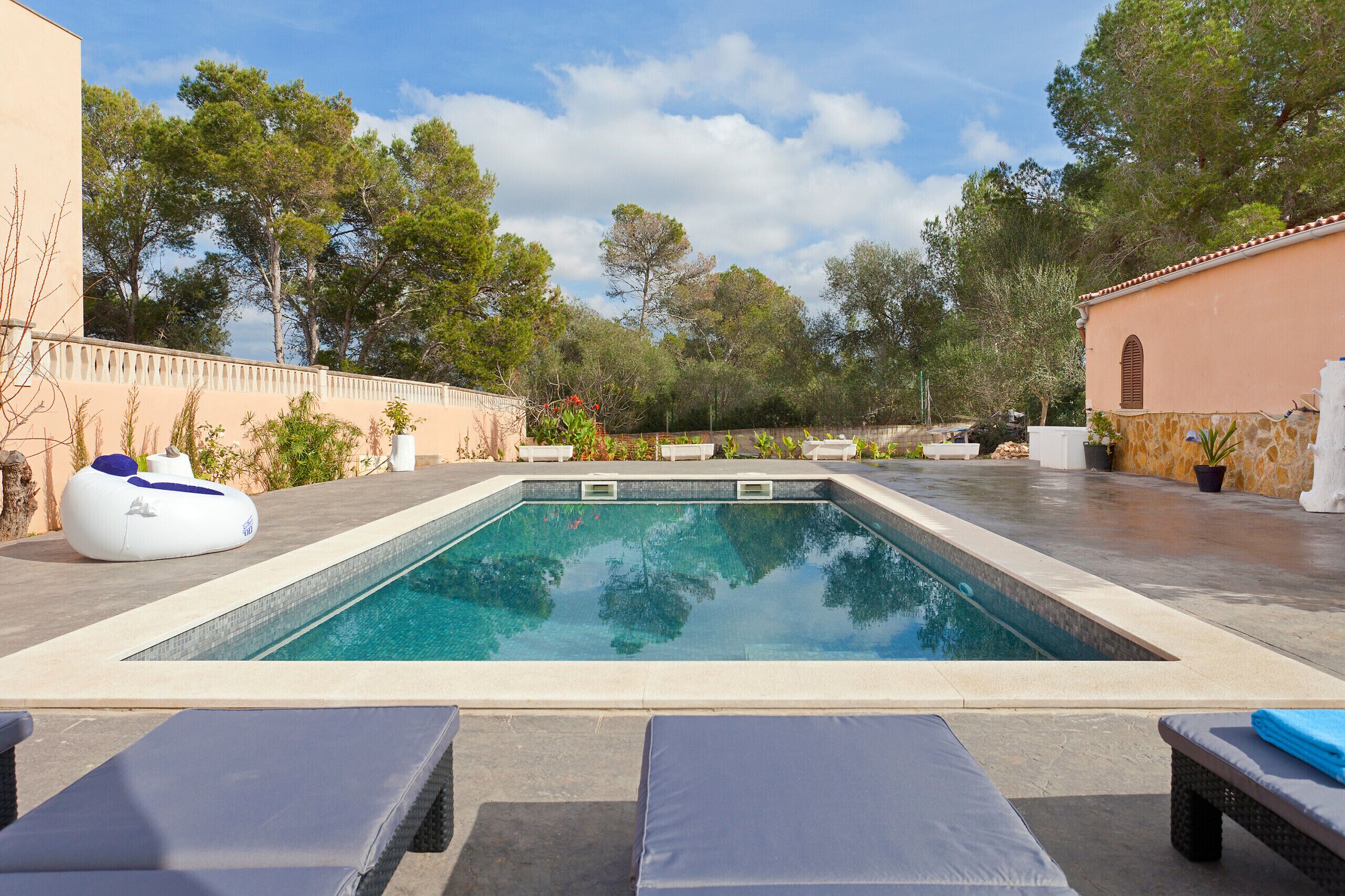A rectangular swimming pool with a tiled deck, surrounded by lounge chairs and a white floating chair.