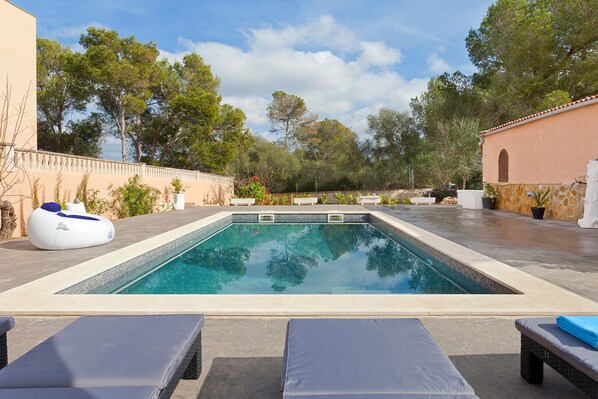 A rectangular swimming pool with a tiled deck, surrounded by lounge chairs and a white floating chair. - Villa Angela - with private swimming pool (Llucmajor)