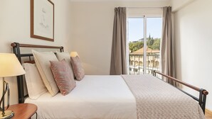 A hotel room with a bed, a nightstand, a lamp, and a view of a building through the window. - Ilhéus III, quiet place in the city center (Funchal)