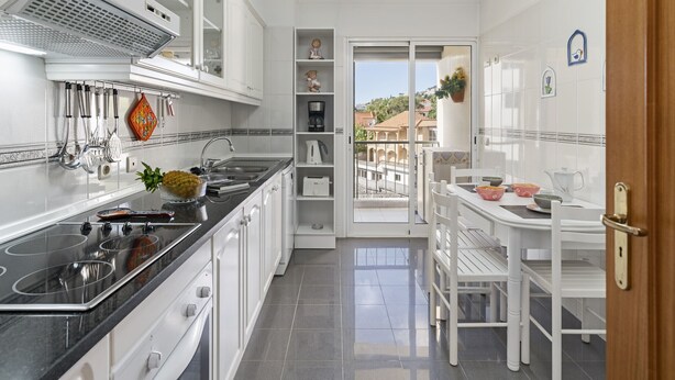 A modern kitchen with white cabinets, a black countertop, and a dining area with white chairs and a table. - Ilhéus III, quiet place in the city center (Funchal)