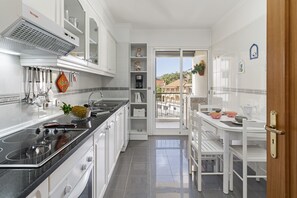 A modern kitchen with white cabinets, a black countertop, and a dining area with white chairs and a table. - Ilhéus III, quiet place in the city center (Funchal)