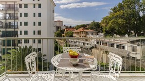 A balcony with a table and chairs, a bowl of fruit, and a book titled "DAQUALI". - Ilhéus III, quiet place in the city center (Funchal)