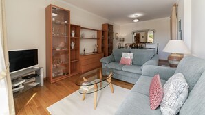 A living room with a sofa, a glass coffee table, a TV, and a wooden cabinet with shelves. - Ilhéus III, quiet place in the city center (Funchal)