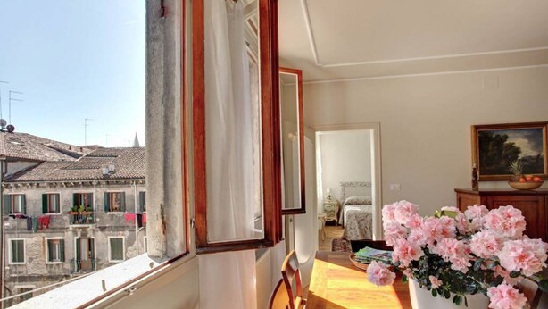 Een kamer met uitzicht op gebouwen, een houten tafel, een kamerplant en een bed.
