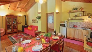 A cozy living room with a dining table set for four, a kitchen area with a microwave and stove, and a red sofa.