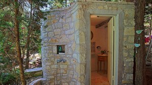 A stone-built outdoor shower area with a stone wall, a small window, and a door leading to an interior bathroom.