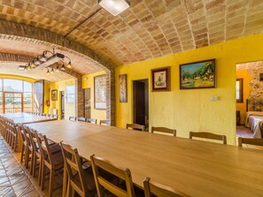 Ein großer Speisesaal mit einem langen Holztisch und Stühlen, einer Ziegeldecke und gelben Wänden.