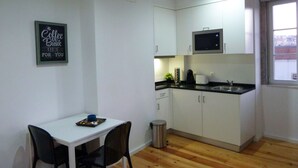 A small, modern kitchen with white cabinets, a microwave, and a sink. There's a framed sign on the wall and a trash can near the sink.