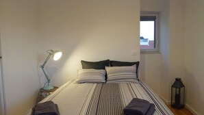 A neatly made bed with striped bedding, two pillows, and two folded towels. There is a desk lamp on the left side of the bed.