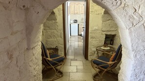 A narrow stone-walled corridor with two wicker chairs and a small table, leading to a kitchen area. - Large trullo/ villa, with private 10x4 m pool, in olive grove 2km from town (Ceglie Messapica)