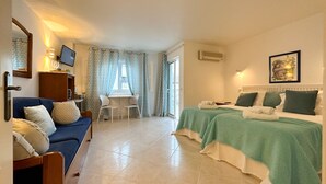 Ein Hotelzimmer mit zwei Betten, einem Schlafsofa, einem Schreibtisch und einem Fenster mit Vorhängen.