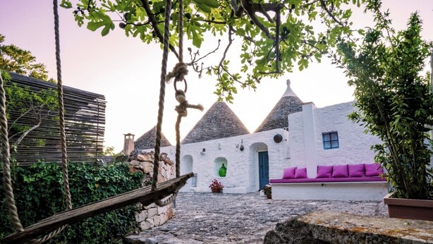 A traditional white-washed building with conical roofs, a stone pathway, and a hammock. - Charming Trullo Amarcord with Private Pool, Spa & Park near Alberobello (Selva di Fasano)