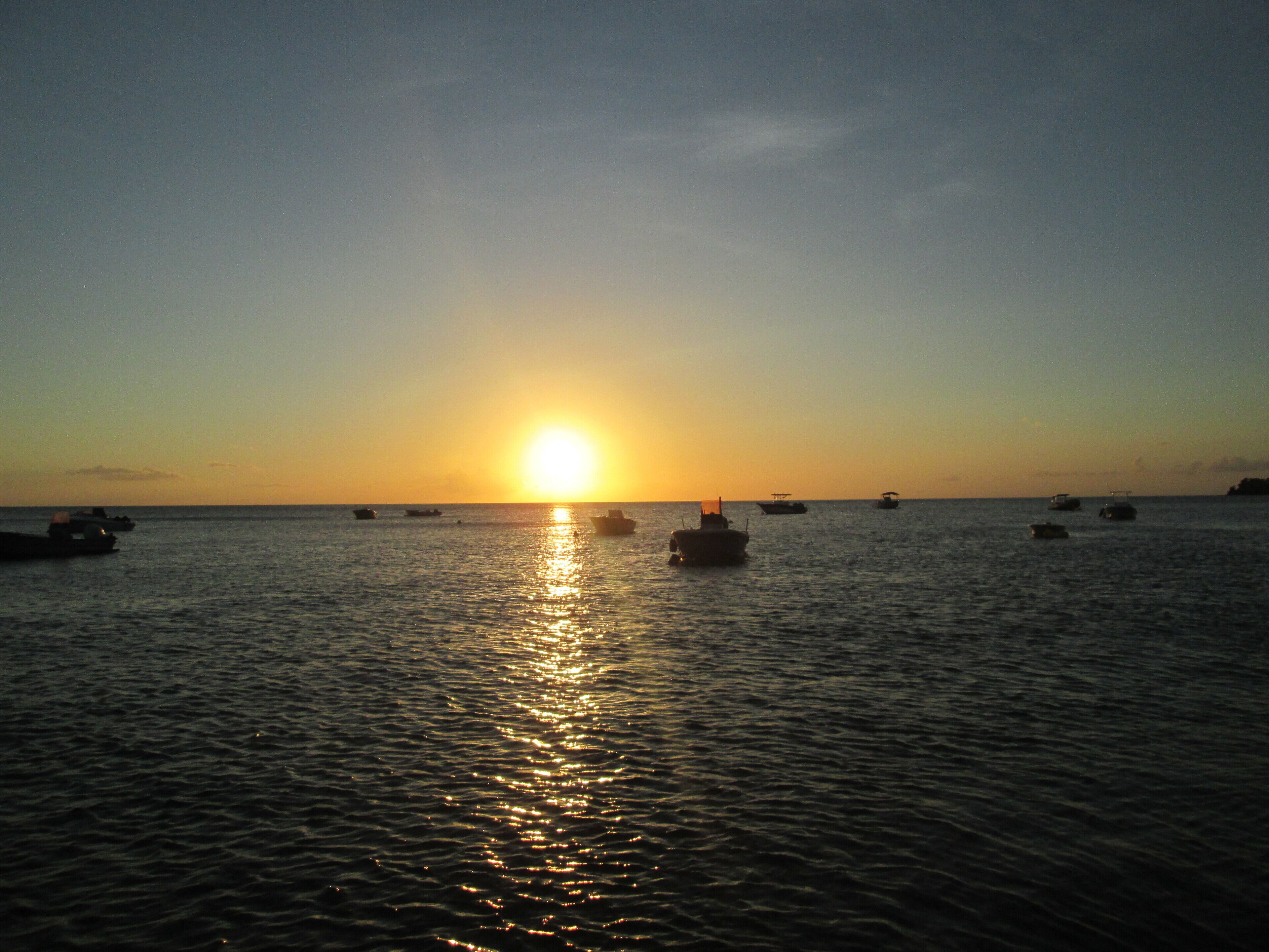 A sunset over a calm sea with several boats.