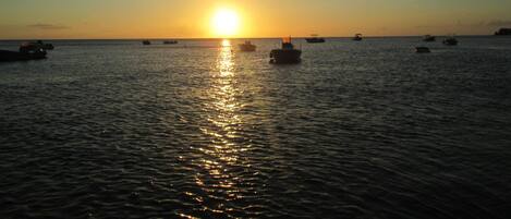 A sunset over a calm sea with several boats.