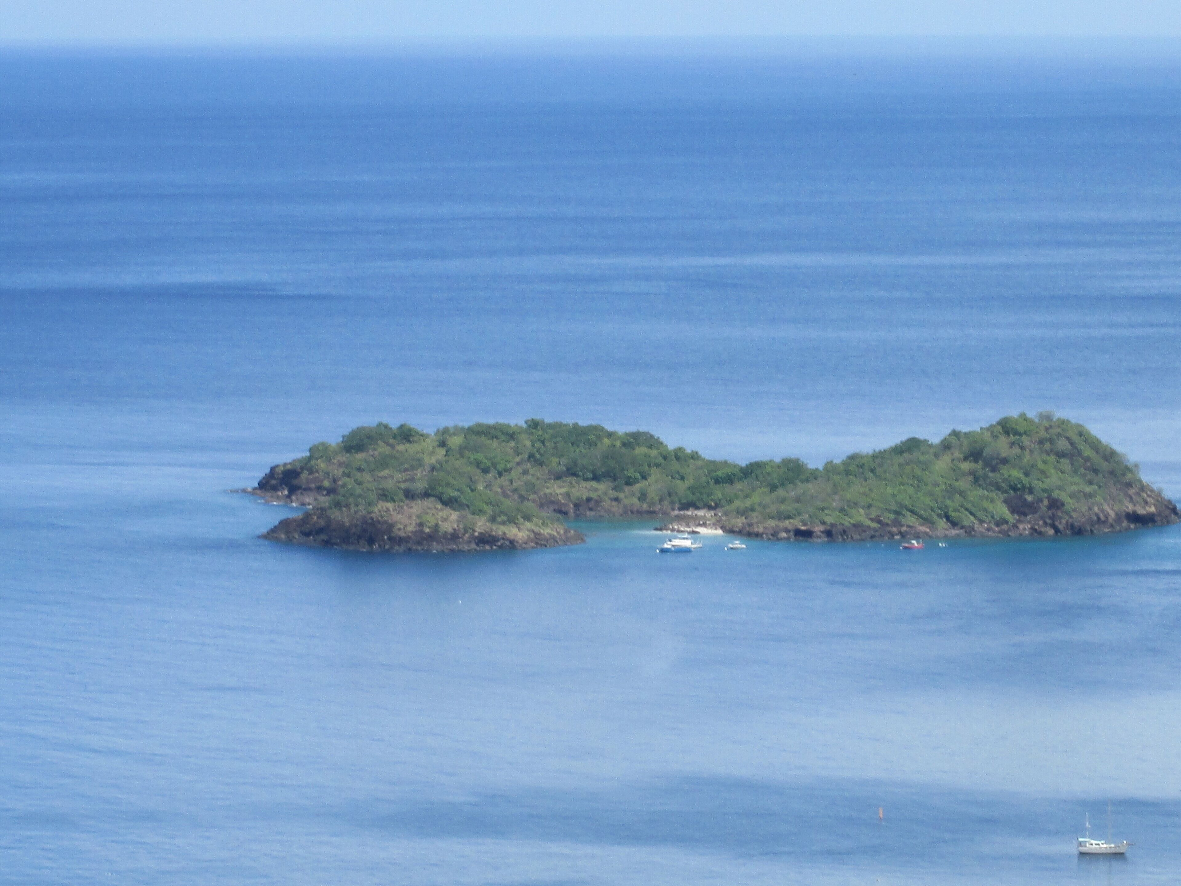A small island with dense green vegetation surrounded by calm blue waters.